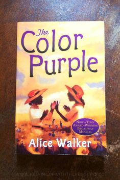 the book cover for the color purple by alice walker on a wooden table with a black and white cat