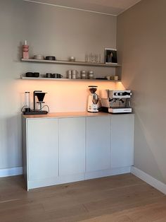 a kitchen with white cupboards and shelves filled with coffee machines on top of them