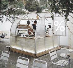 two people sitting at a counter in a small glass building with white chairs around it