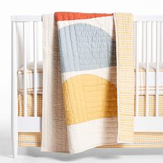 a white crib with a yellow, blue and orange quilted blanket on it