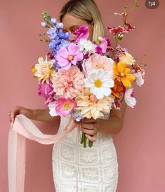 a woman holding a bouquet of flowers in front of her face and wearing a white dress