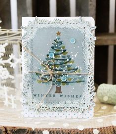 a card with a christmas tree on it sitting on top of a table next to snowflakes