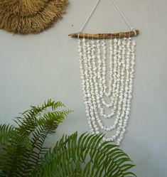 a white beaded wall hanging next to a plant