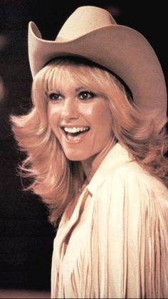 a woman with blonde hair wearing a cowboy hat and looking at the camera while standing in front of a microphone