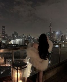 a woman standing on top of a building looking at the city lights in the distance