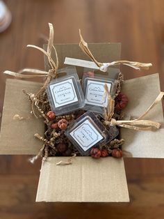 three square candles sitting on top of a cardboard box with dried berries and pine cones