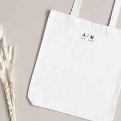 a white shopping bag sitting on top of a table next to some dried flowers and a plant