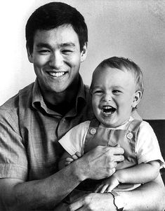 a black and white photo of a man holding a laughing baby in his lap,