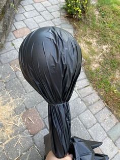 a hand holding a black plastic bag over it's head on the side of a sidewalk