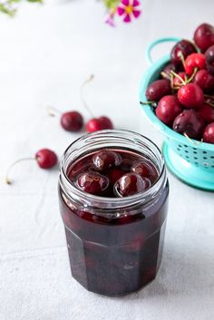 a glass jar filled with cherries sitting on top of a table next to a basket of cherries