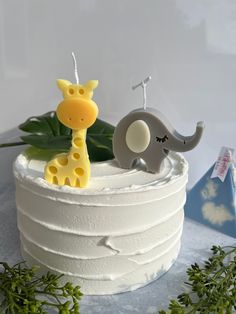 two giraffes and an elephant sitting on top of a white cake with greenery