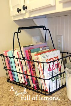 a basket filled with books sitting on top of a counter next to a white cabinet