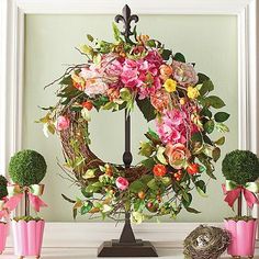 a wreath with pink and yellow flowers on top of a mantle next to vases