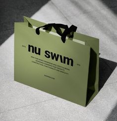 a green shopping bag with the words nu swim printed on it and a black ribbon