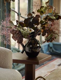 a vase filled with flowers sitting on top of a wooden table next to a white chair