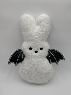 a white stuffed animal with a black bat on it's back and wings spread out