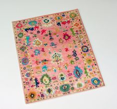 a pink rug with many different colored designs on the top and bottom, sitting on a white surface