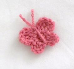 a crocheted pink flower on a white surface with some yarn in the shape of a heart