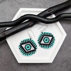 a pair of blue and black beaded earrings on top of a white hexagonal plate