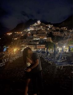 a man and woman kissing in front of a city at night with the lights on