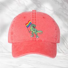 "Dinosaur Rainbow Flag Hat, T-Rex LGBTQ Hat, LGBTQ+ Pride Cap, Pride Parade Hat, LGBTQ Support Cap, Pride Month Gift, Colorful Equality Hat Hats comes with black design only We use DTF Vinyl Heat Pressed Design. Mega Cap - Pigment Dyed Cotton Twill Cap - 7601A - 100% cotton pigment dyed twill - Unstructured, six-panel, low profile - Self-fabric sweatband and six sewn eyelets - Self-fabric strap with brass snap buckle and sewn grommet - Adult Sizing: 6 5/8\" - 7 3/8\"" Playful Adjustable Dad Hat With Curved Brim, Fun Adjustable Dad Hat, Novelty Snapback Hat, Fun Visor Dad Hat, Fun Dad Hat With Visor, Fun Dad Hat With Visor, One Size Fits Most, Novelty Baseball Cap With Adjustable Curved Brim, Red Novelty Hat One Size, Novelty Adjustable Baseball Cap With Curved Brim