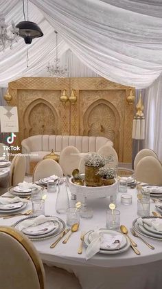 a table set up with plates and silverware in front of a white drape