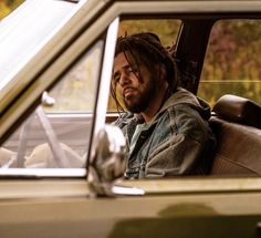 a man with dreadlocks sitting in the back seat of a car looking at something