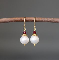 "Lustrous and opalescent white freshwater Akoya pearls are wire wrapped with balled gold pins and topped with gold caps and faceted Red Ruby stones. These dangle from gold balled earwires. These classic pearl earrings are a wonderful addition to any jewelry wardrobe and are perfect to give as bridal gifts. Multiple pairs can be ordered. A matching pendant is also available. Want these in a different color? Please send a message! Red Ruby stones: 3mm Akoya pearls: 10mm Total length of earrings: 1 White Elegant Earrings For Festive Occasions, Elegant White Earrings For Festive Occasions, Red Pearl Drop Round Earrings, Red Round Pearl Drop Earrings, Elegant White Gemstone Pearl Earrings, White Elegant Pearl Earrings, Red Pearl Drop Earrings, Elegant Festive Earrings With Round Beads, Festive White Pearl Drop Earrings