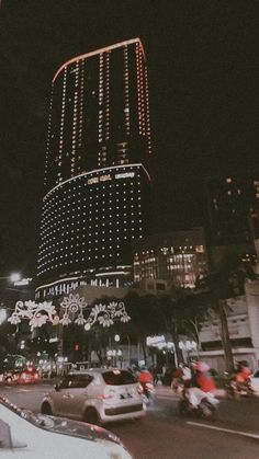 cars and motorcycles are driving down the street at night in front of a tall building