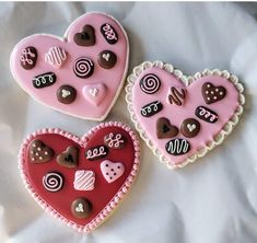 three decorated heart shaped cookies sitting on top of a white sheet