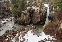 an aerial view of a waterfall surrounded by rocks and trees in the snow covered mountains