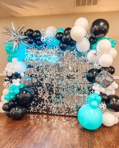 a table topped with balloons and black and white decorations on top of a wooden floor