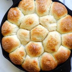 a cast iron skillet filled with rolls on top of a white counter next to a cup of coffee