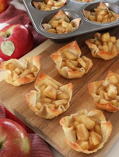 apple pies are sitting on a cutting board next to apples and muffin tins