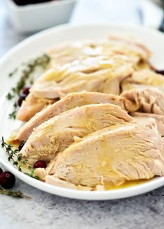 sliced chicken on a white plate with cranberries and herbs around the edges, ready to be eaten