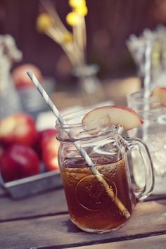 two mason jars filled with apple cider on top of a wooden table next to apples