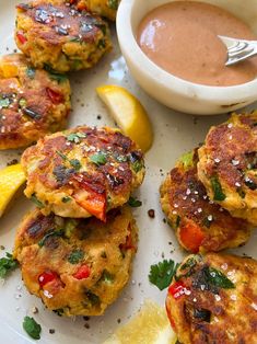 several crab cakes on a white plate with lemon wedges and sauce in the background