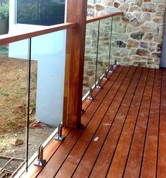 a wooden deck with glass railing and stone wall