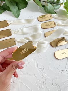 gold name tags are being held up by someone's hand on a white surface