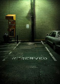 an empty parking lot next to a green brick wall with a pay here sign on it