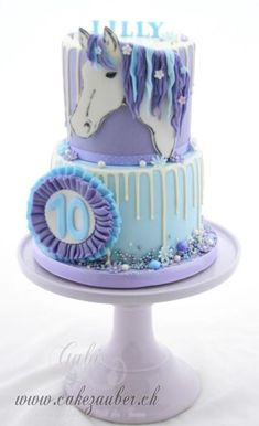 two tiered cake decorated with blue and purple icing and a horse on top