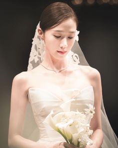 a woman in a white wedding dress holding a bouquet of flowers and wearing a veil