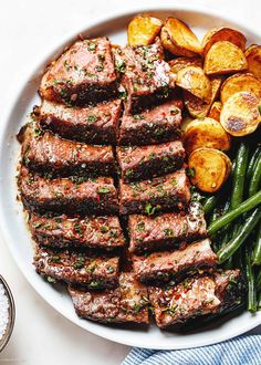 a white plate topped with meat and potatoes next to green beans on top of a table