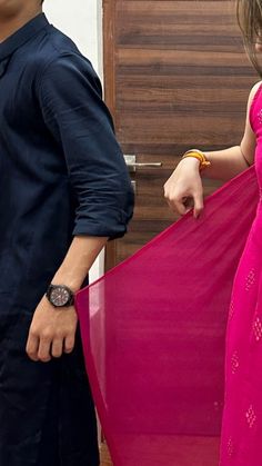 a man and woman standing next to each other in front of a wooden door holding a pink dress