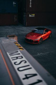 a red sports car parked in front of a shipping container at an industrial area with the word ausra written on it