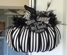 a black and white striped pumpkin hanging from the front door with a sign on it