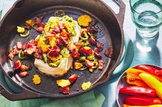 an iron skillet filled with vegetables and meats next to water glasses on a table