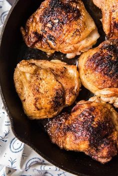 chicken thighs cooking in a skillet on top of a table with blue and white cloth