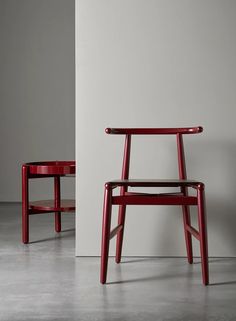 two red chairs sitting next to each other on top of a cement floor in front of a white wall