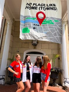 three girls standing in front of a no place like home town sign on a building